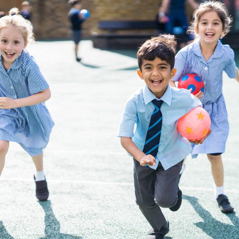 3 students holding balls running towards the playground