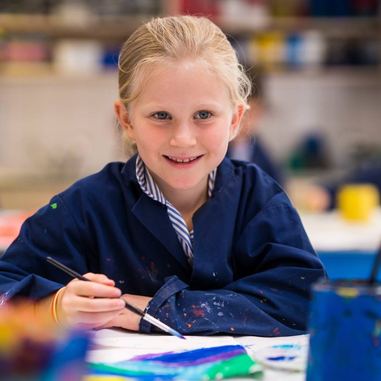 Student holding a paintbrush as they paint onto a piece of paper