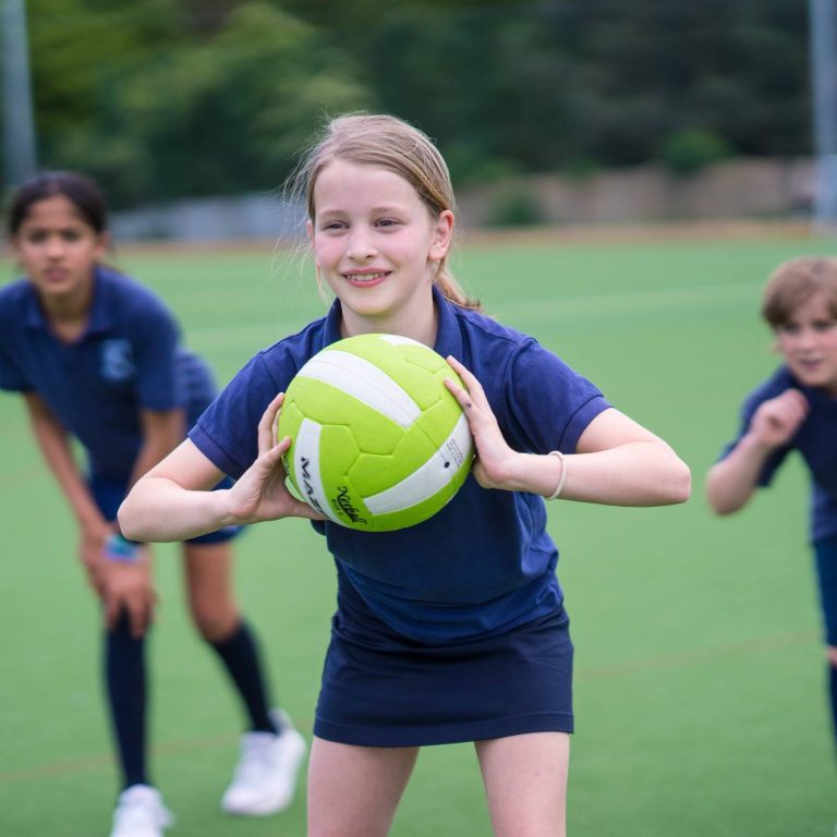 Student with a ball in their hands, about to sent to another player. 2 students are in the background looking on in preparation