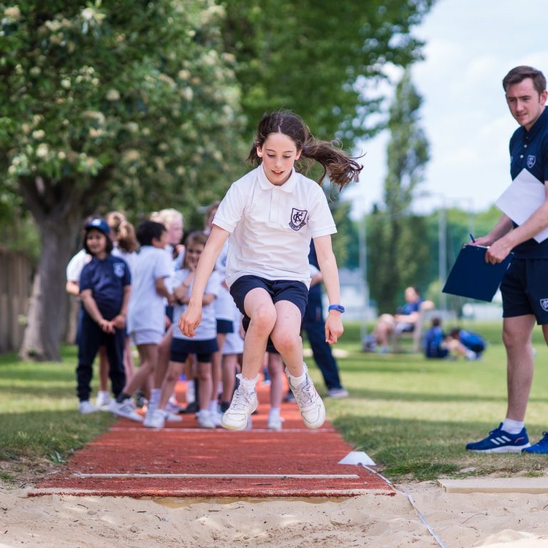 Student jumping on the long jump section as a PE teacher looks on to make a note of the score