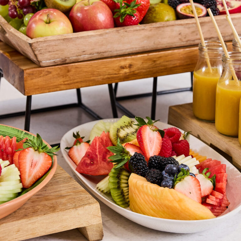 Assorted fresh fruit platter with berries, kiwi, melon slices, and apples on a wooden tray.